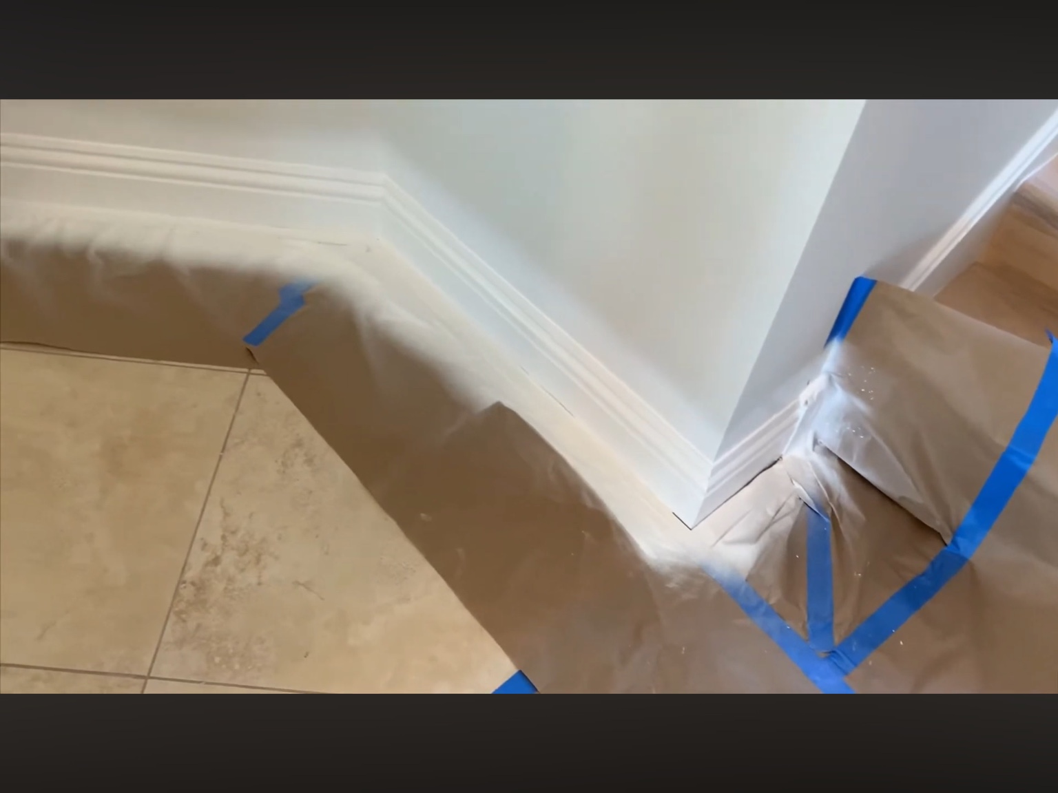 White baseboard corner with paper and blue tape protecting the floor