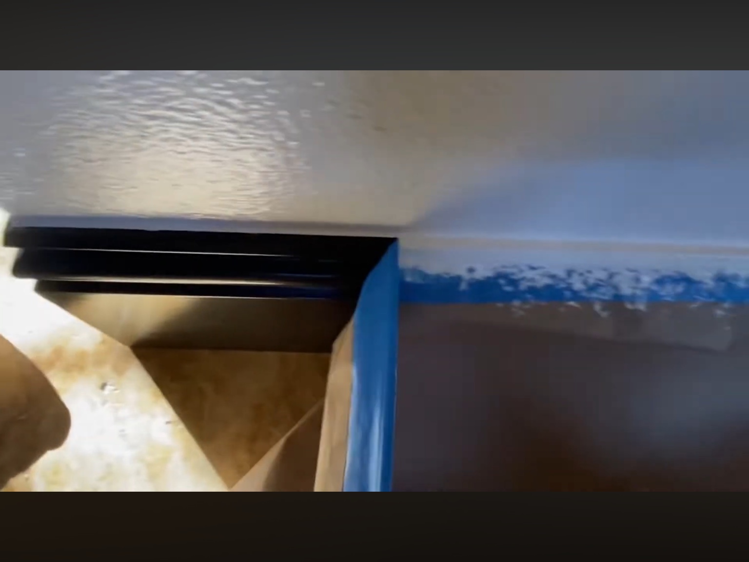 Blue tape being removed to reveal black baseboards against light walls